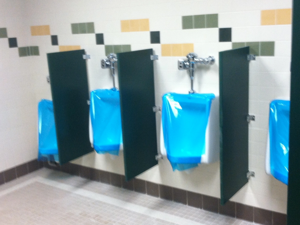 A row of urinals with blue bags on the wall.